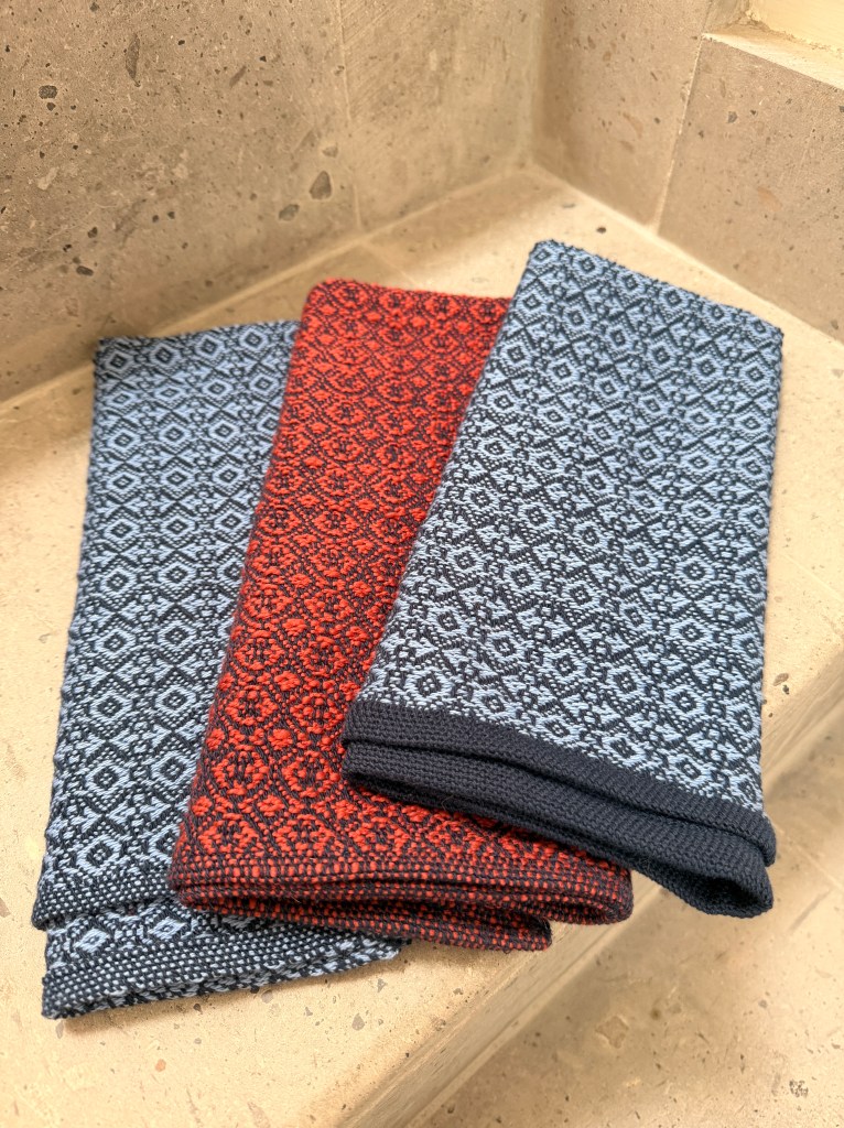 Three handwoven diamond-pattern towels in blue-grey and orange-red