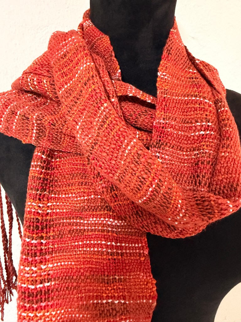 Handwoven orange-red scarf with white accent threads on a black mannequin